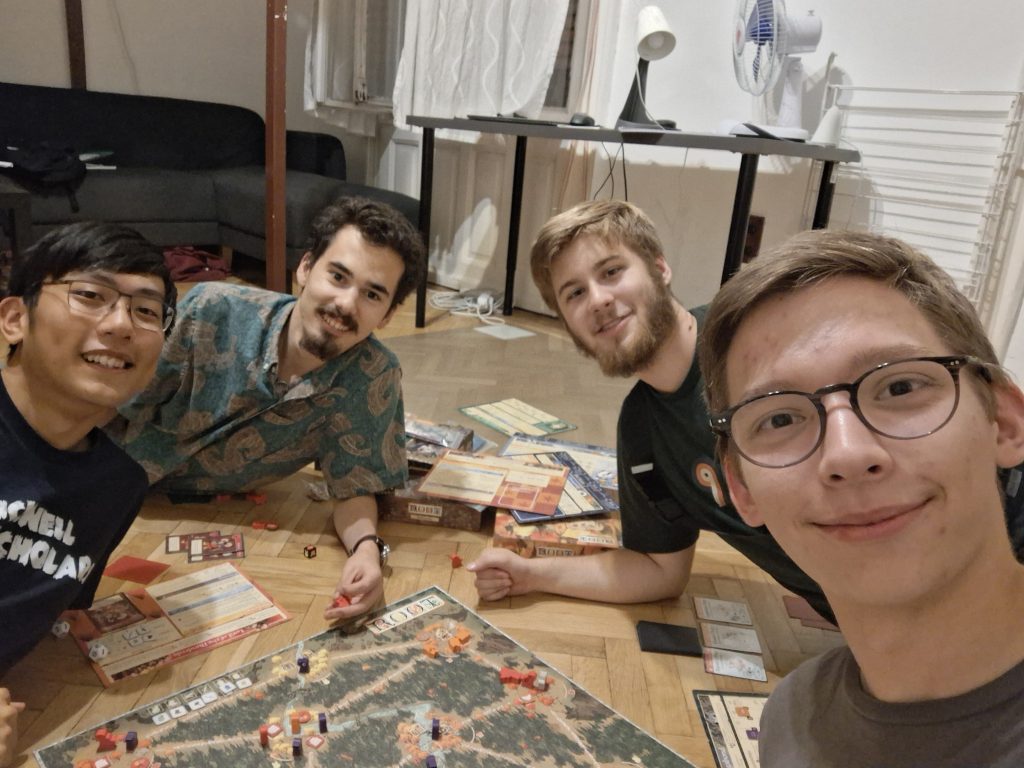 Sam, Skyler, and Sam's friends Benjamin and Nathan playing a board game called Root in Sam's apartment.