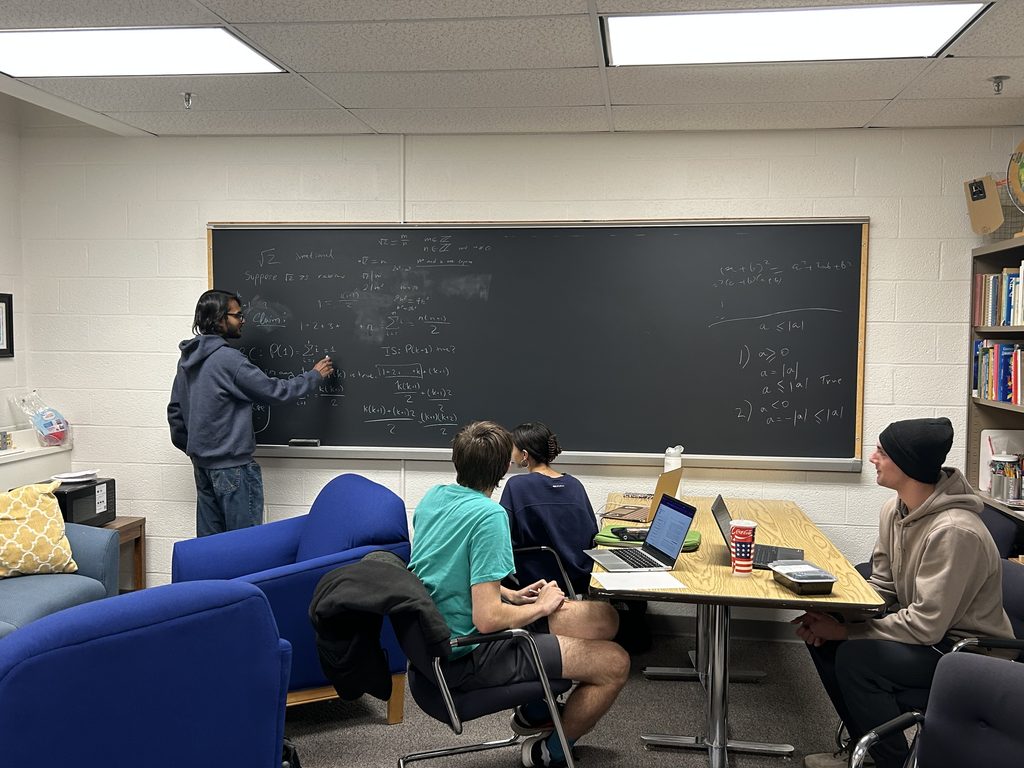 Meshkat works on a math problem at the board while three students listen.