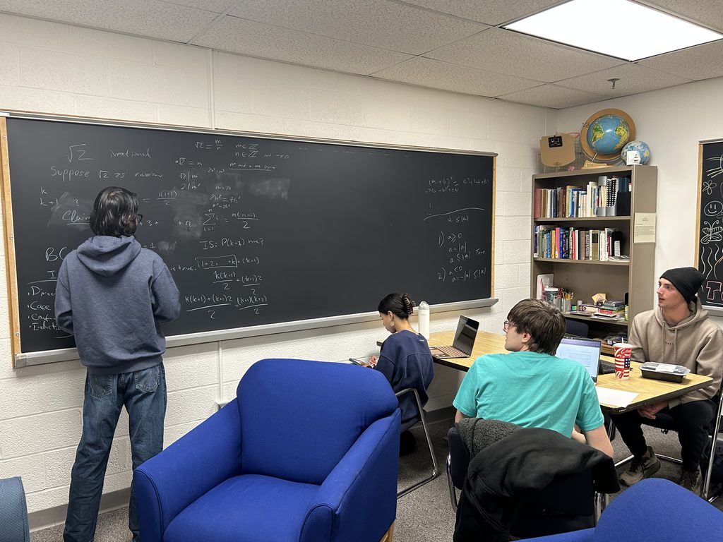 Meshkat works on a math problem at the board while three students listen.